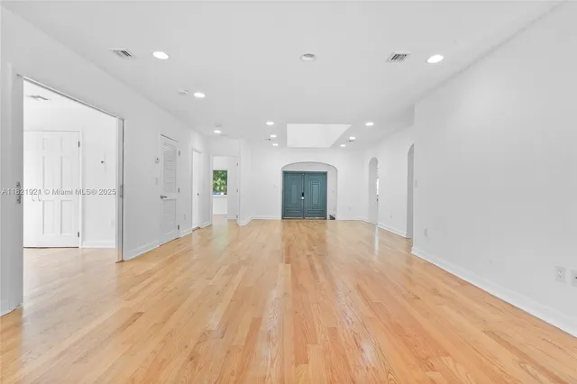 a view of an empty room with wooden floor and a kitchen