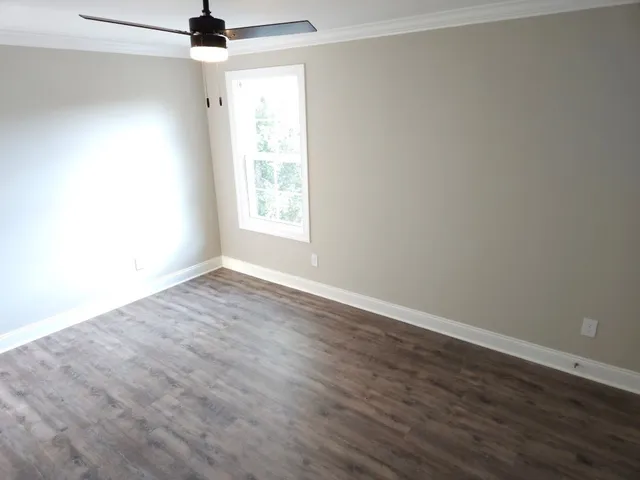 an empty room with wooden floor fan and windows