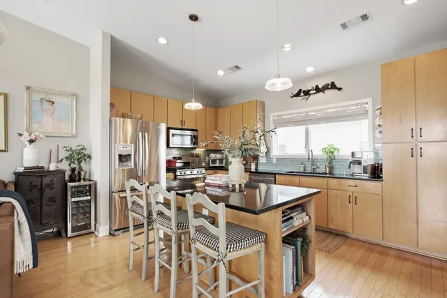 a kitchen with stainless steel appliances kitchen island granite countertop a refrigerator a stove a sink a dining table and chairs with wooden floor