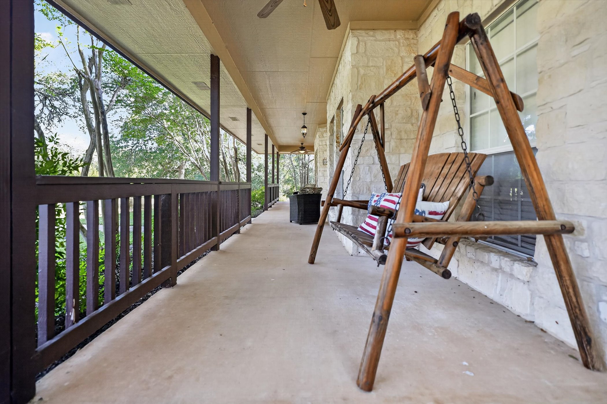 13615 Copperleaf Trail Manchaca, TX 78652 - Photo 5 of 38 A spacious covered porch features a porch swing and stone exterior, providing a tranquil outdoor retreat.