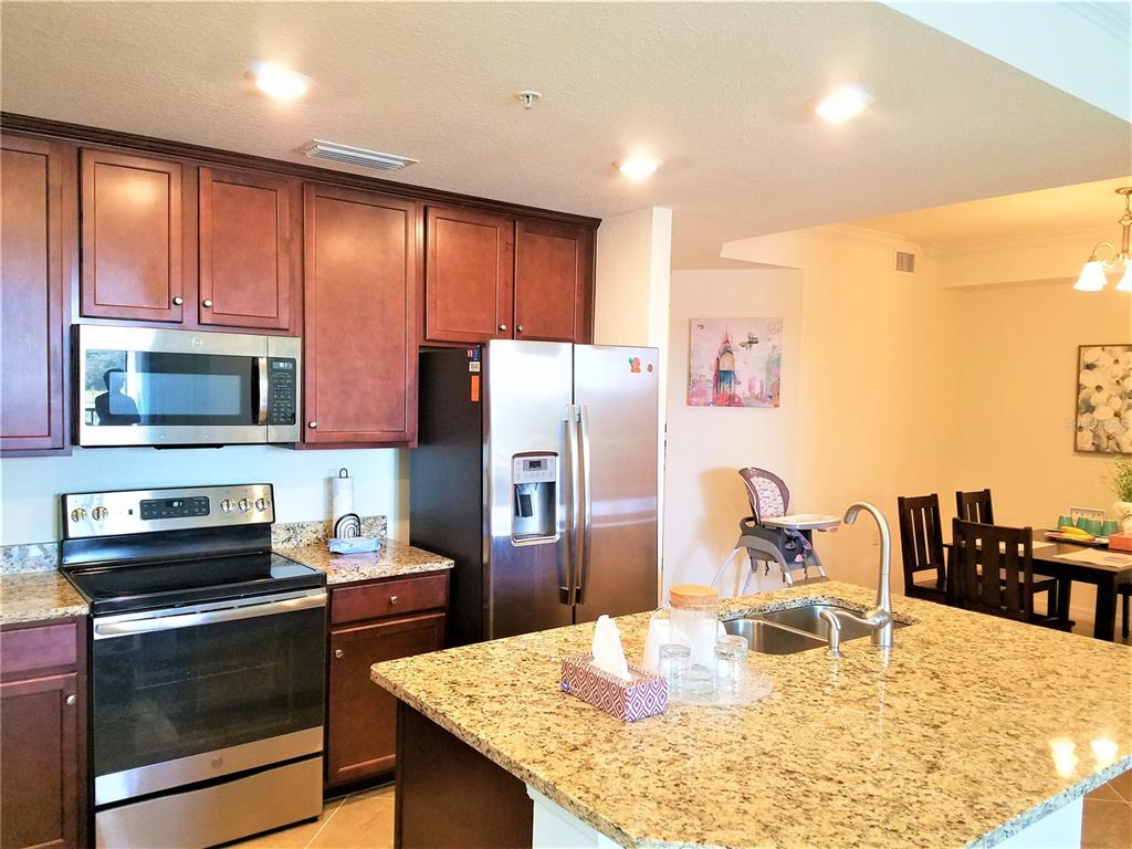 17108 Vardon Terrace, Unit 208 Lakewood Ranch, FL 34211 - Photo 4 of 14 a kitchen with stainless steel appliances granite countertop a refrigerator a stove top oven a sink a dining table and chairs with wooden floor