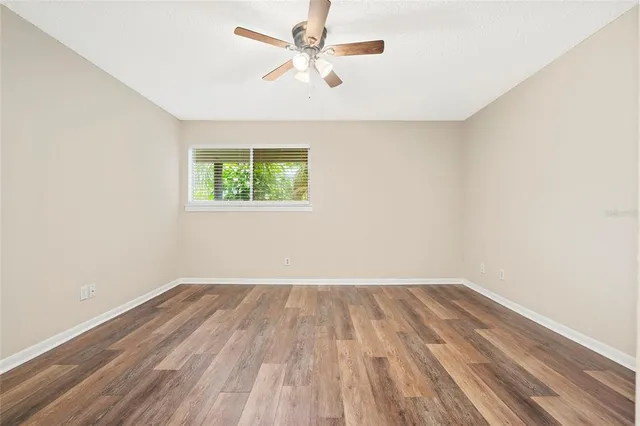 an empty room with wooden floor chandelier fan and windows