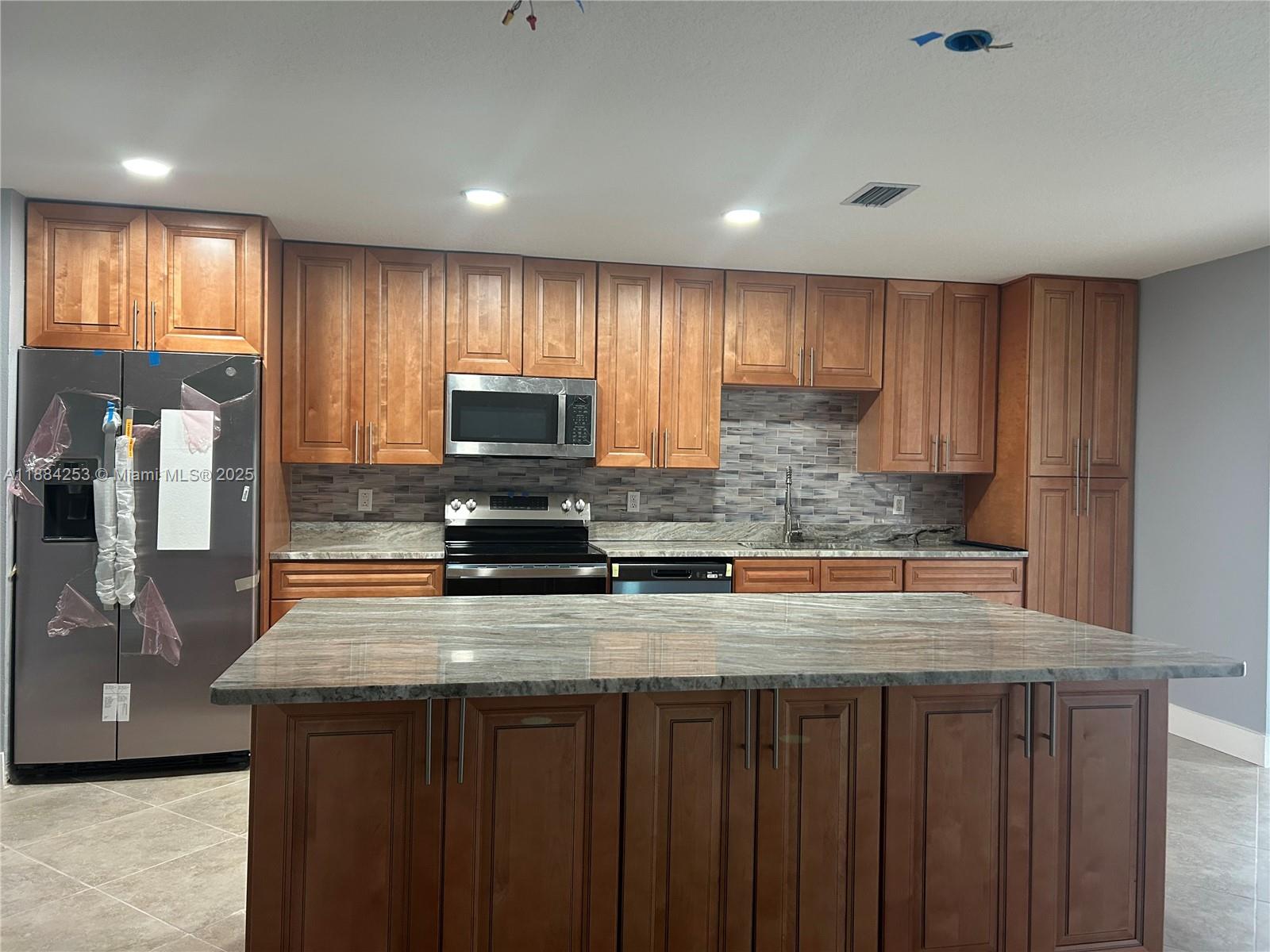 7109 Santa Rosa Parkway Fort Pierce, FL 34951 - Photo 3 of 11 a kitchen with kitchen island granite countertop wooden cabinets a refrigerator and a sink