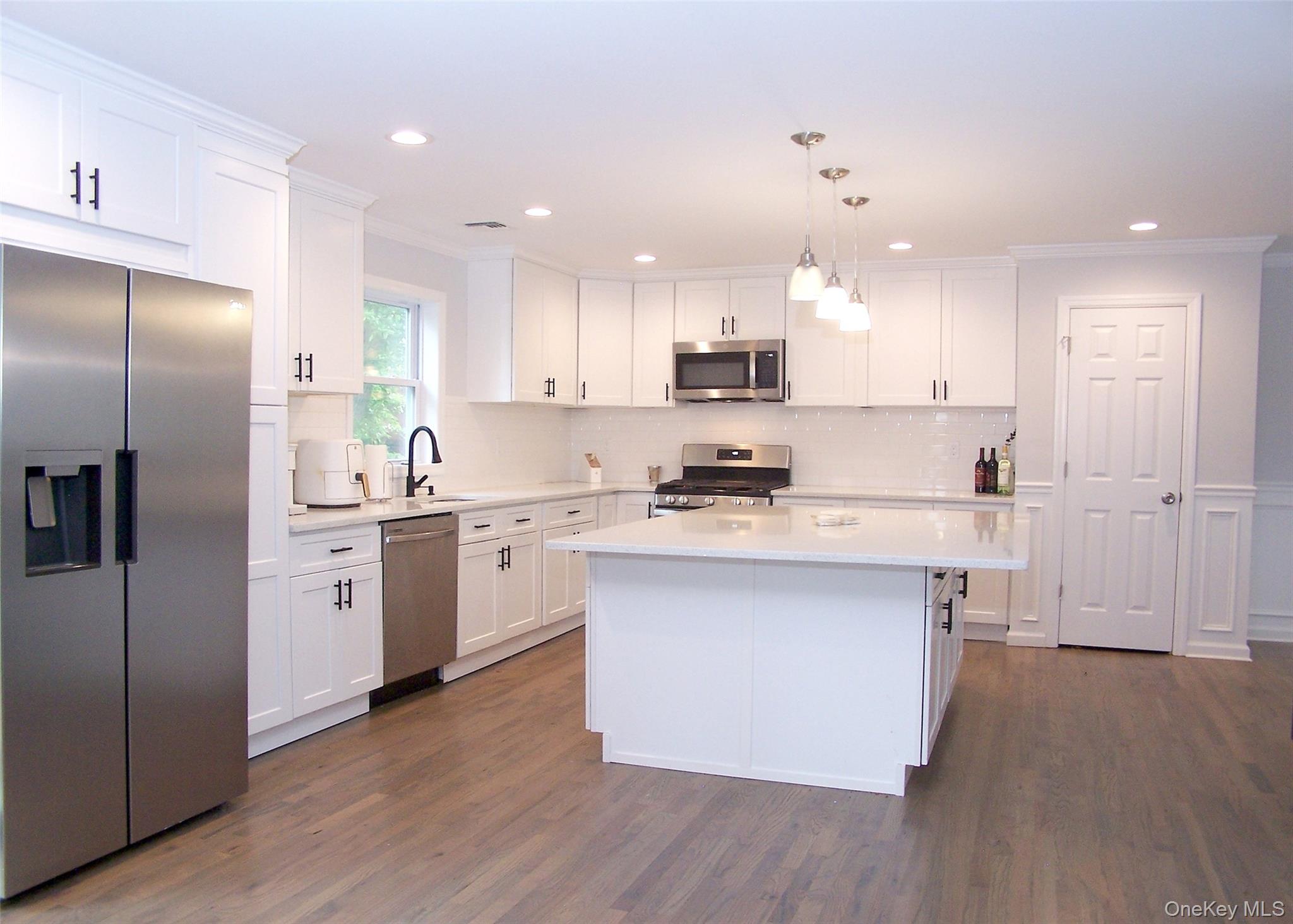 8 Narcissus Road Mastic Beach, NY 11951 - Photo 9 of 20 a kitchen with white cabinets stainless steel appliances and wooden floor