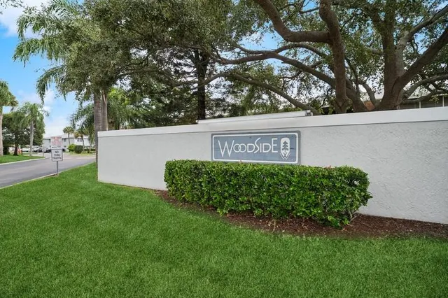 a view of a sign in a yard with potted plants and large trees