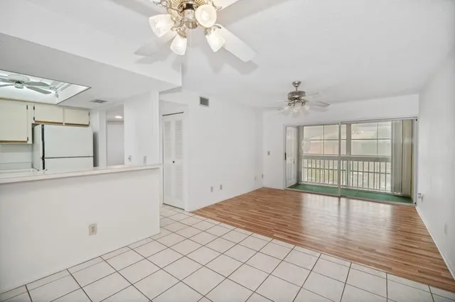 a view of an empty room with chandelier fan and kitchen view