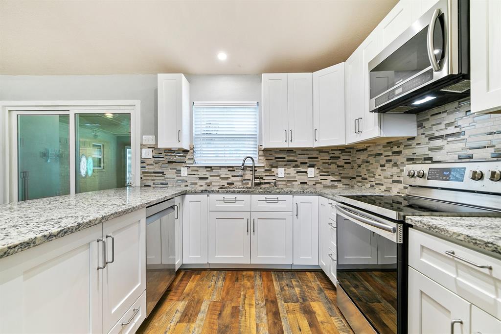 909 North Dove Road Grapevine, TX 76051 - Photo 8 of 30 Kitchen featuring white shaker cabinetry, speckled countertops, a mosaic tile backsplash, stainless steel appliances, and wood-finish flooring
