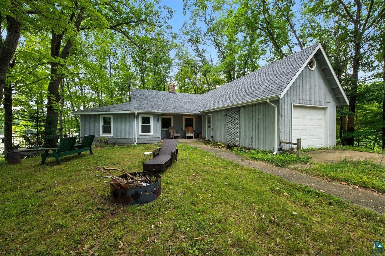 Single story home with a fire pit, a garage, concrete driveway, a chimney, and roof with shingles