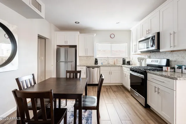 a kitchen with stainless steel appliances granite countertop a stove a refrigerator a kitchen island a dining table and chairs with wooden floor
