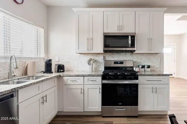 a kitchen with stainless steel appliances granite countertop grey cabinets a stove a sink and a microwave