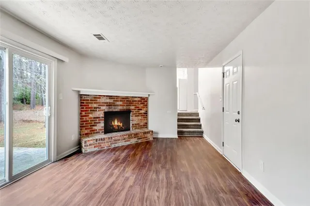 a view of an empty room with wooden floor fireplace and a window