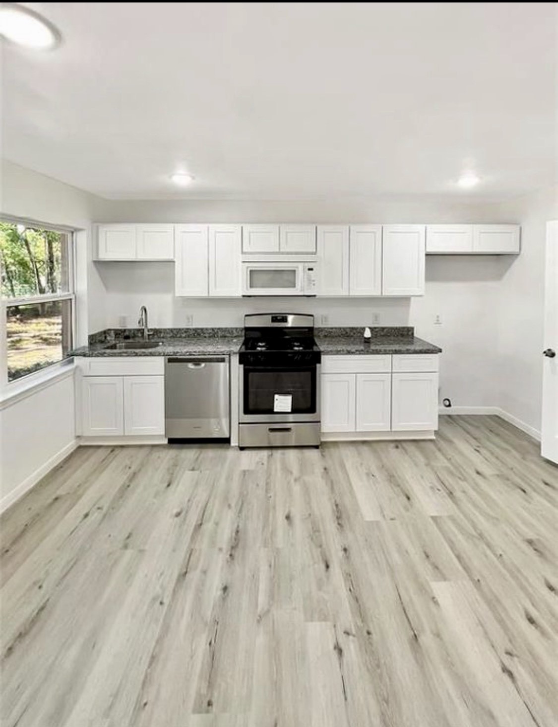 408 Commanche Road Conroe, TX 77316 - Photo 5 of 25 Bright and modern kitchen featuring sleek white cabinetry, stainless steel appliances, and elegant granite countertops, complemented by light wood flooring.