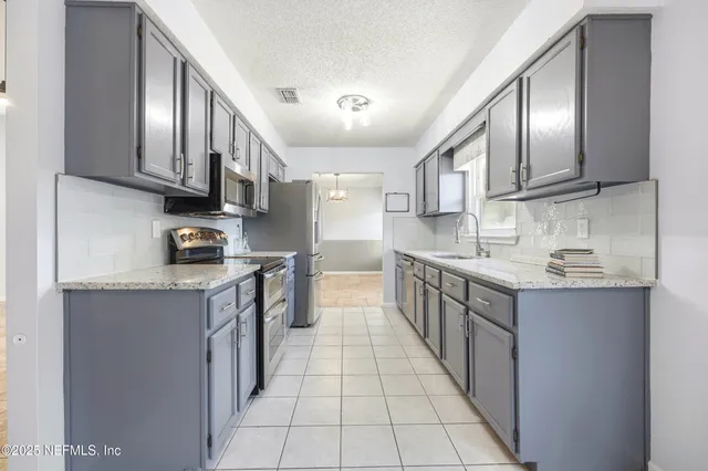 a kitchen with stainless steel appliances granite countertop a sink a stove top oven a refrigerator with grey cabinets