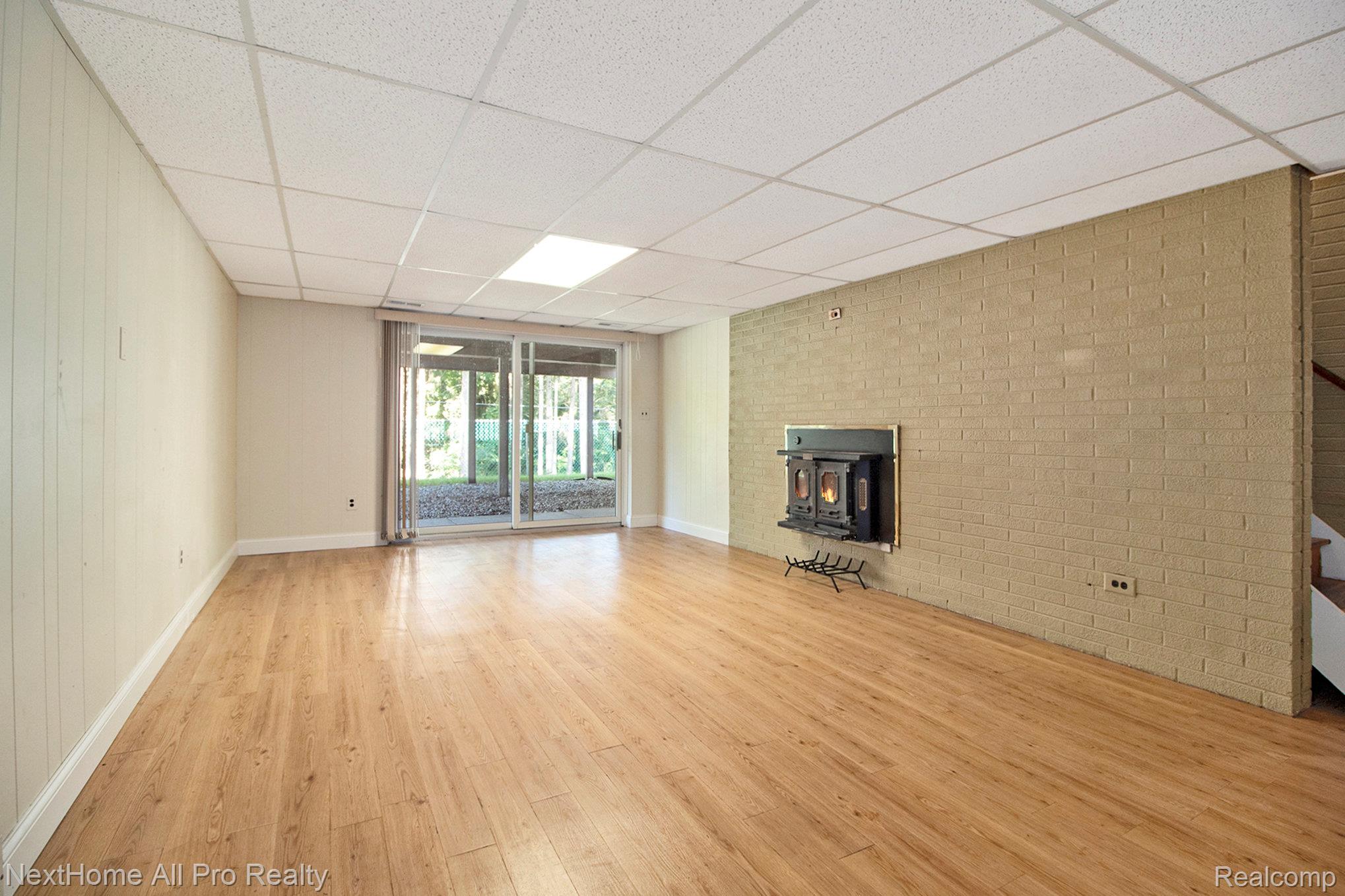 7195 Curtis Road Northville, MI 48168 - Photo 39 of 70 Lower Level Family Room featuring a wood stove and sliding glass door leading to patio with fenced yard.