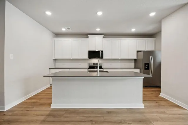 a kitchen with stainless steel appliances kitchen island granite countertop a dining table chairs refrigerator and microwave