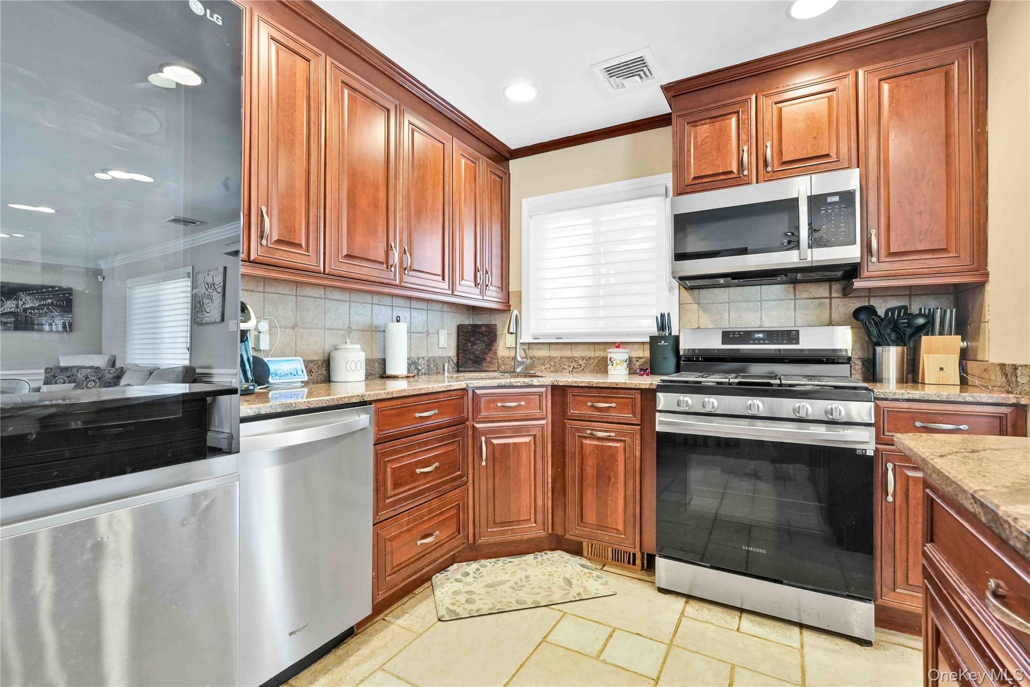 2 Amherst Lane Smithtown, NY 11787 - Photo 12 of 33 Kitchen with crown molding, appliances with stainless steel finishes, light stone countertops, backsplash, and brown cabinets