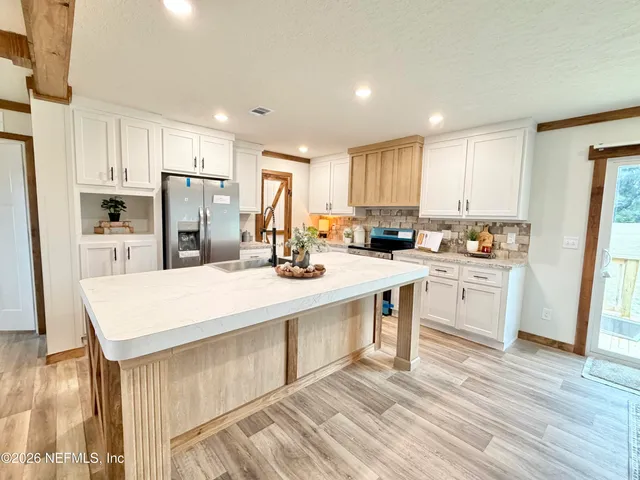 a kitchen with kitchen island a sink a stove a refrigerator and white cabinets with wooden floor