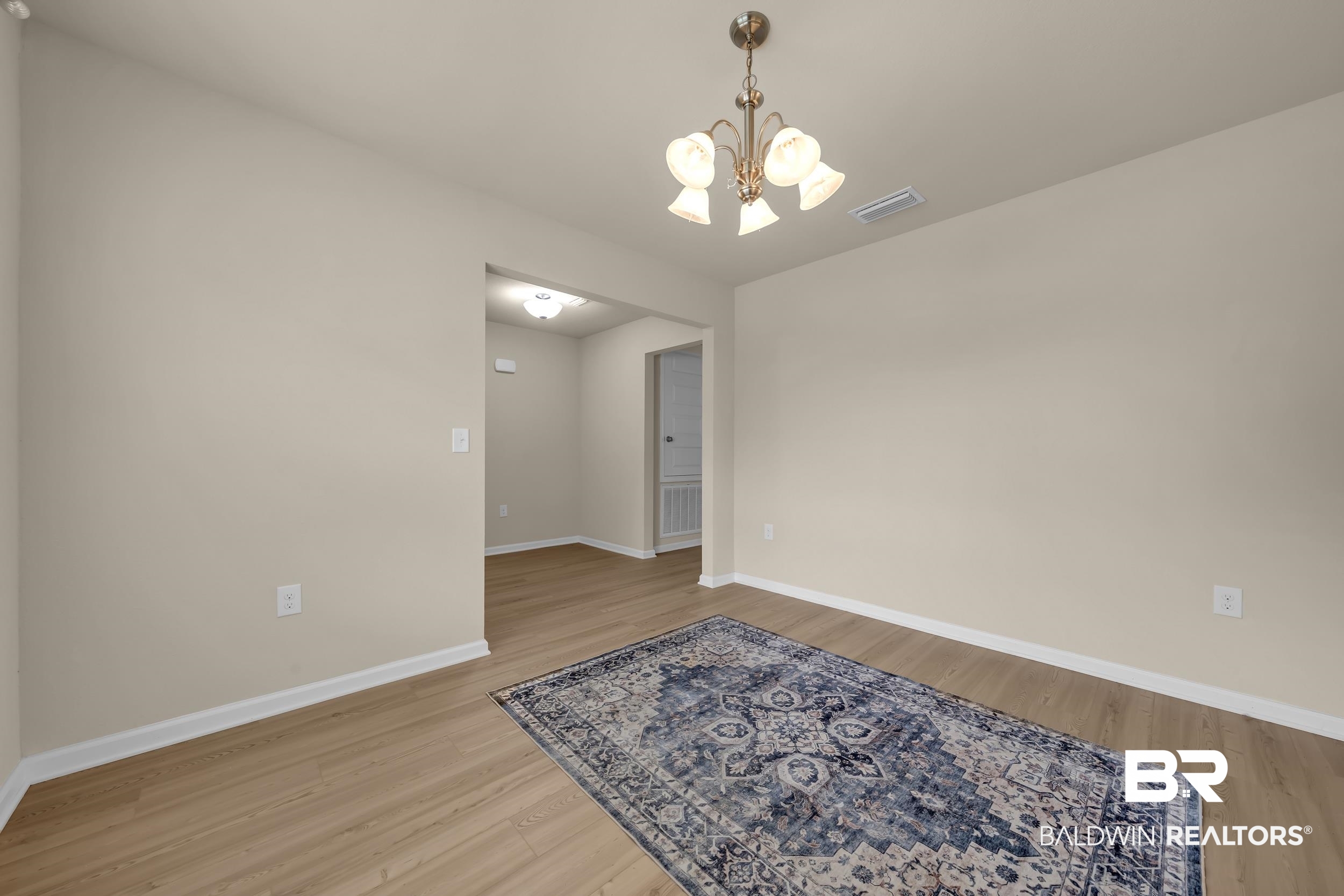 1704 Abbey Loop Foley, AL 36535 - Photo 6 of 38 Spacious room featuring wood-finish flooring, light neutral wall tones, white baseboards, and an overhead chandelier with frosted glass shades