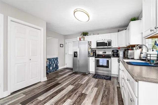 a kitchen with stainless steel appliances granite countertop a refrigerator oven a sink dishwasher and white cabinets with wooden floor