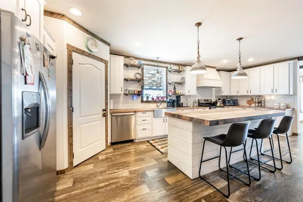 a kitchen with stainless steel appliances kitchen island granite countertop a refrigerator a oven a sink and white cabinets with wooden floor