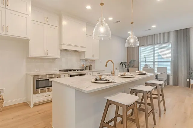 a kitchen with stainless steel appliances granite countertop a sink a stove a refrigerator and white cabinets with wooden floor