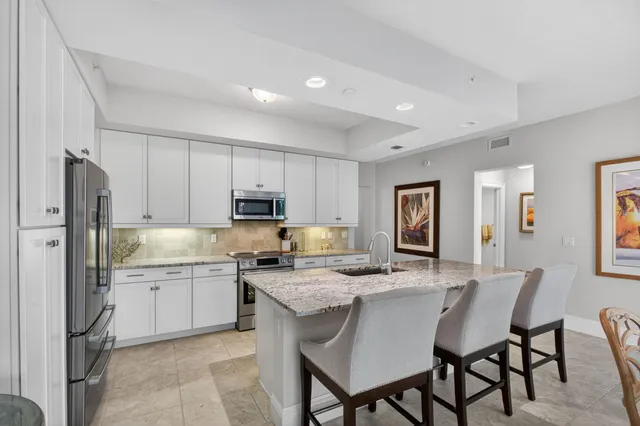 a open kitchen with stainless steel appliances granite countertop a stove top oven a sink a refrigerator and a dining table