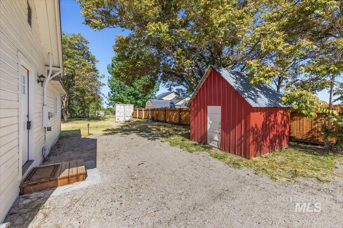 109 Parma Road Parma, ID 83660 - Photo 25 of 31 Spacious backyard featuring a red storage shed with a metal roof, a wooden privacy fence, mature trees, and a gravel area
