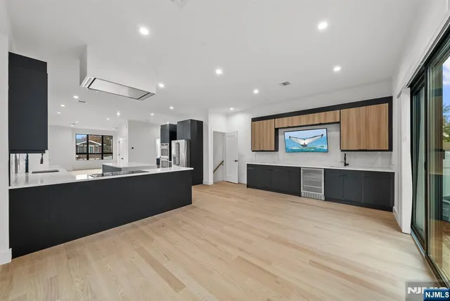 a large kitchen with stainless steel appliances a sink dishwasher a refrigerator and white cabinets with wooden floor