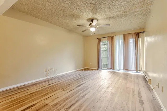 an empty room with wooden floor chandelier fan and windows