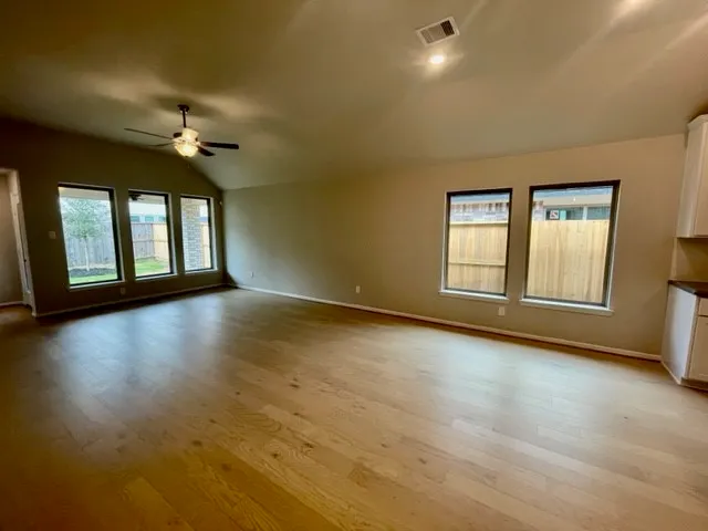 an empty room with wooden floor chandelier fan and windows
