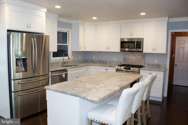 a kitchen with stainless steel appliances granite countertop a refrigerator a stove a sink a microwave and white cabinets with wooden floor