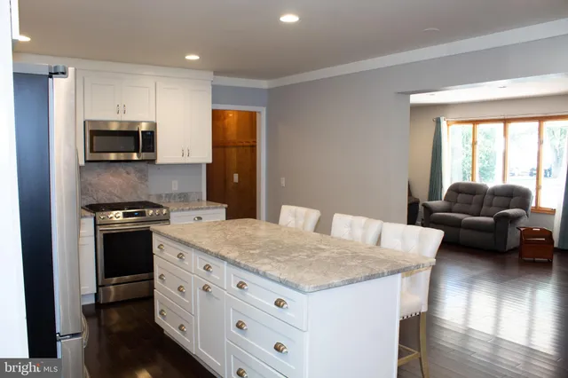 a kitchen with stainless steel appliances granite countertop a stove top oven a sink dishwasher a refrigerator and a dining table with wooden floor
