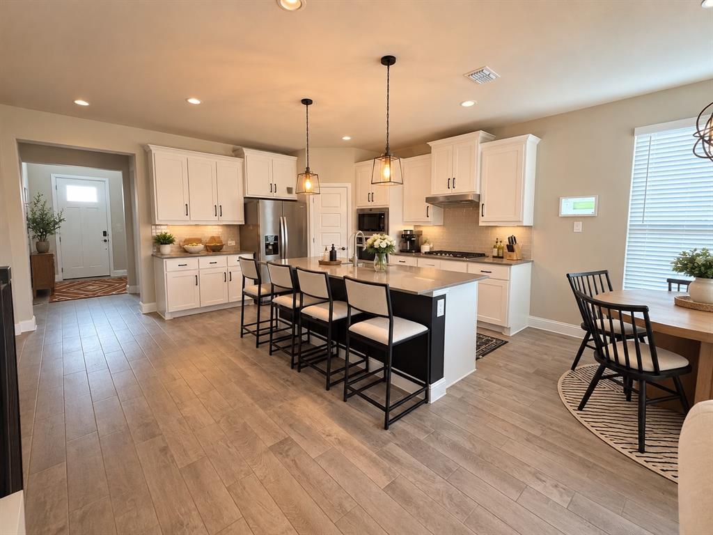 1605 Buzzard Road Denton, TX 76205 - Photo 9 of 27 Open-concept kitchen featuring white cabinetry, a large kitchen island with dark base, stainless steel appliances, and light wood-finish flooring