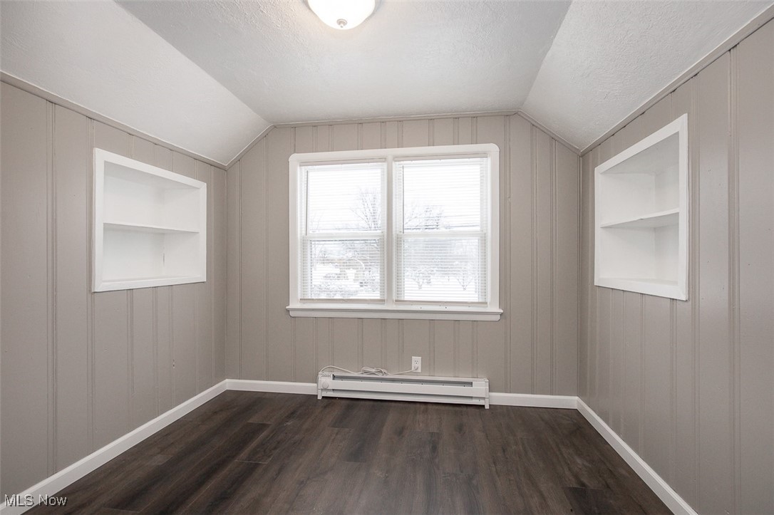 12328 Granger Road Cleveland, OH 44125 - Photo 27 of 37 Additional living space featuring built in shelves, dark wood-style floors, a baseboard radiator, a textured ceiling, and vaulted ceiling