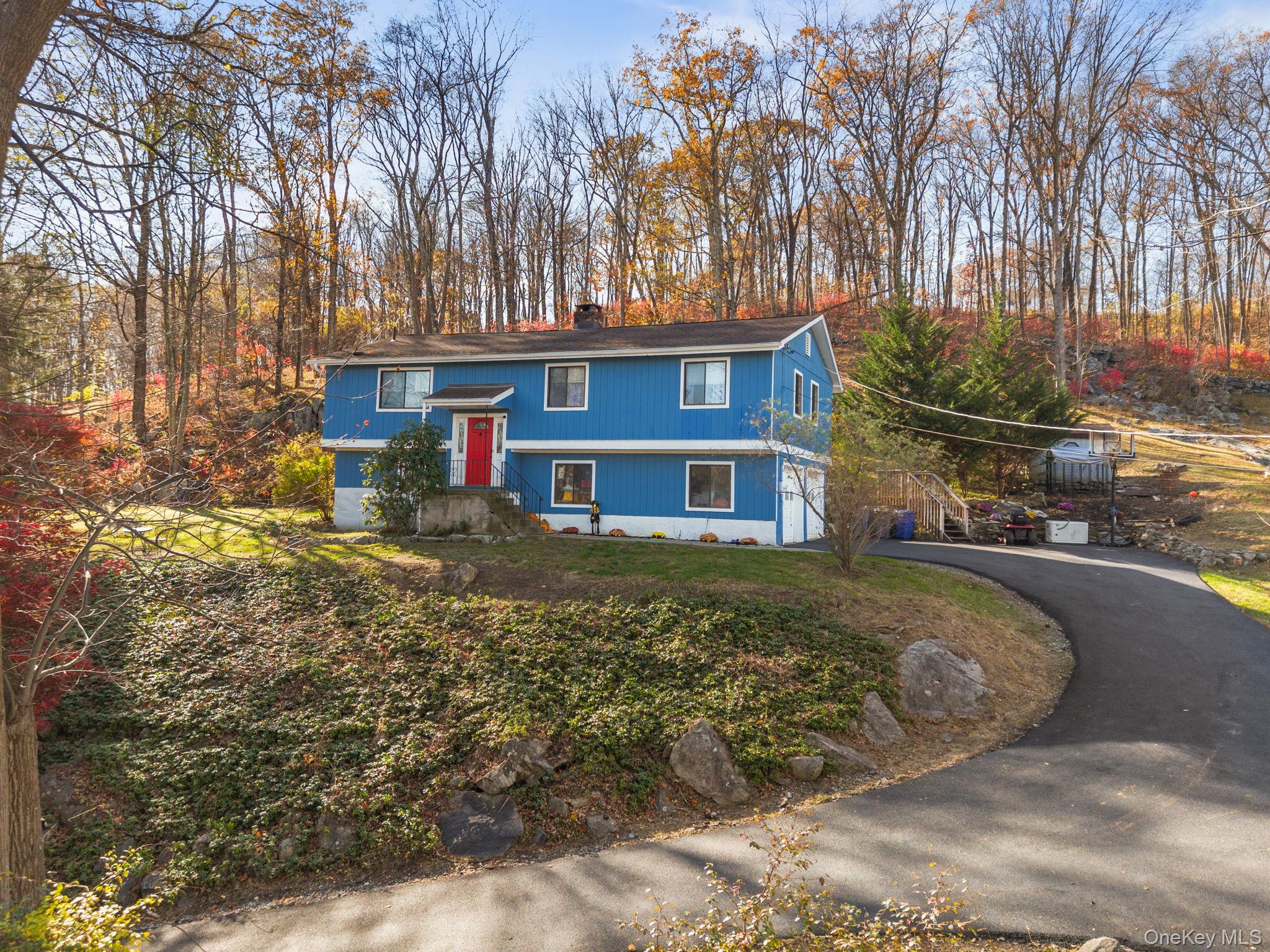 Raised ranch with driveway, a chimney, view of wooded area, and a garage