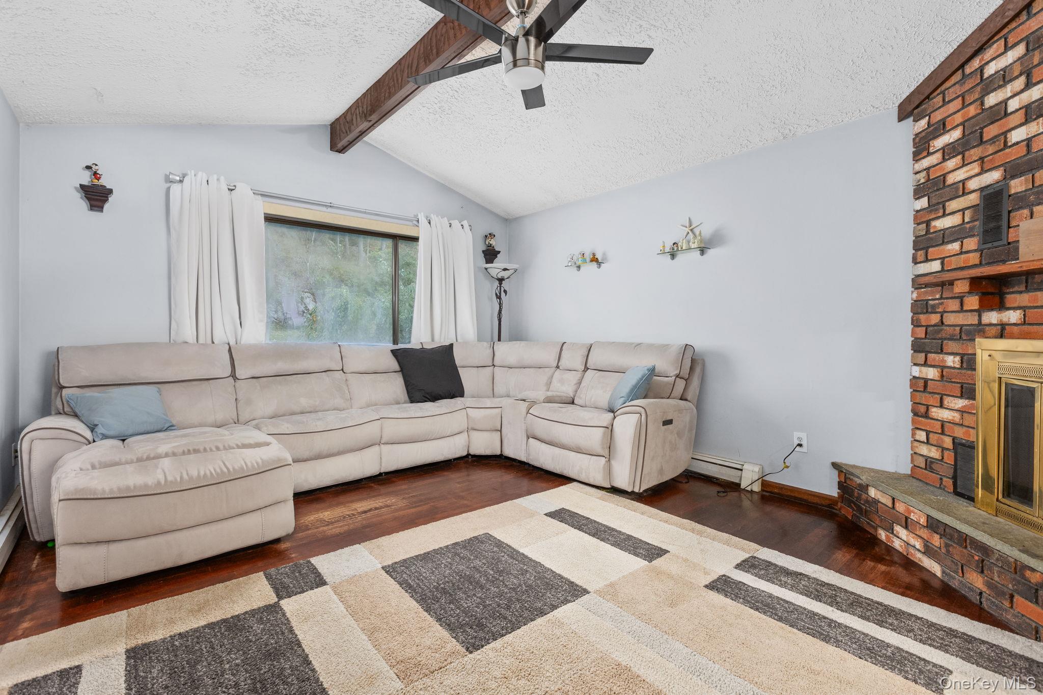 97 Old Road Brewster, NY 10509 - Photo 12 of 23 Living area featuring a textured ceiling, a fireplace, wood finished floors, a ceiling fan, and a baseboard heating unit