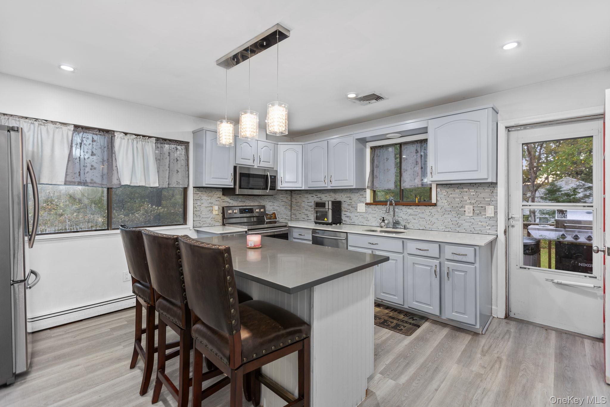 97 Old Road Brewster, NY 10509 - Photo 5 of 23 Kitchen with gray cabinets, decorative backsplash, decorative light fixtures, appliances with stainless steel finishes, and light wood-style flooring