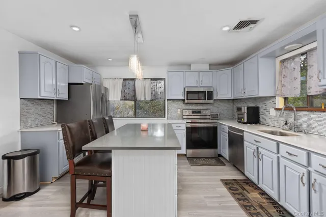 a kitchen with kitchen island granite countertop a stove top oven a sink dishwasher a refrigerator and white cabinets with wooden floor