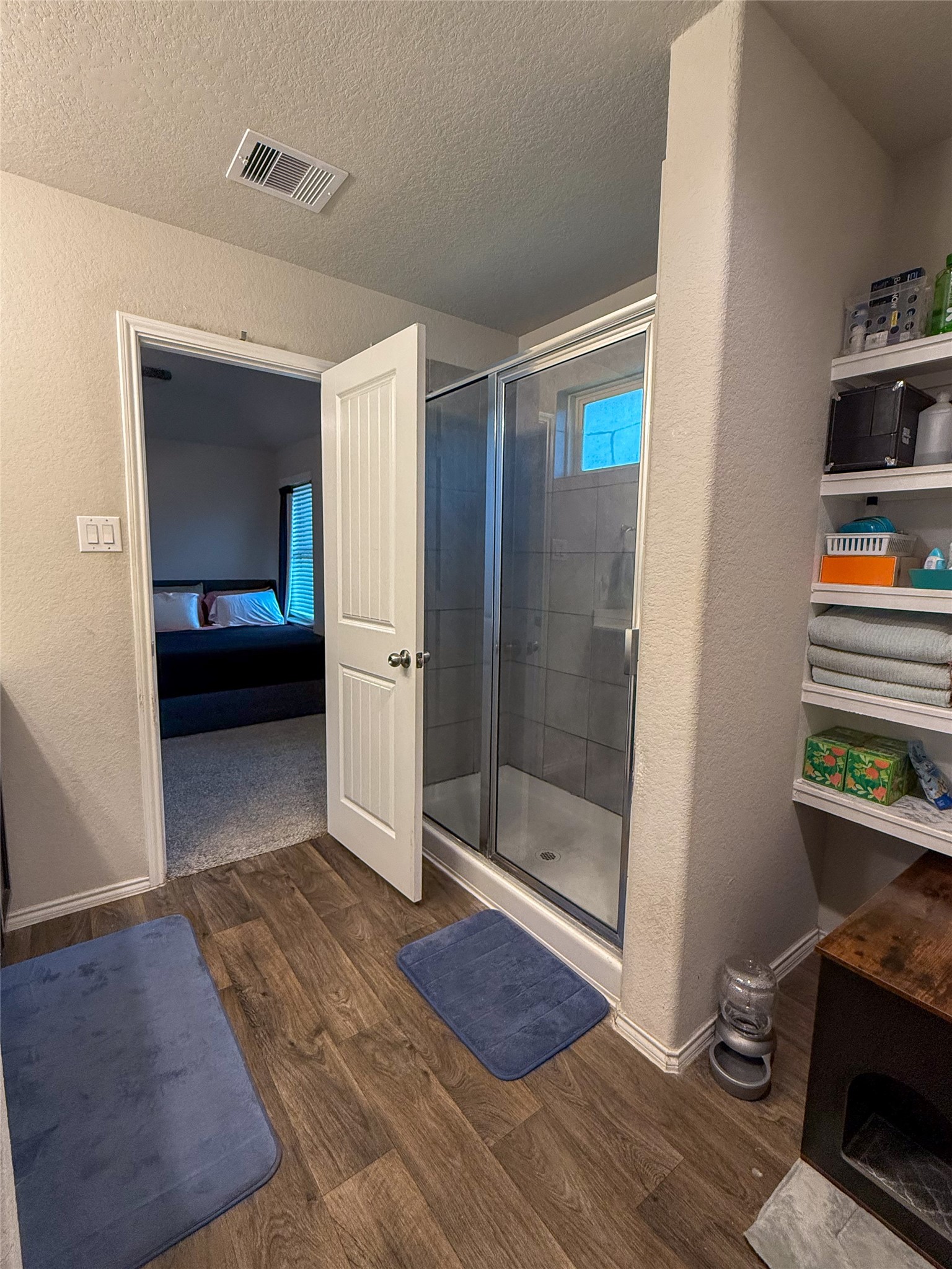 706 Zinnia Court Rosharon, TX 77583 - Photo 11 of 13 This photo shows the primary bathroom featuring a glass-enclosed shower with tiled walls, wood-style flooring, and open shelving.