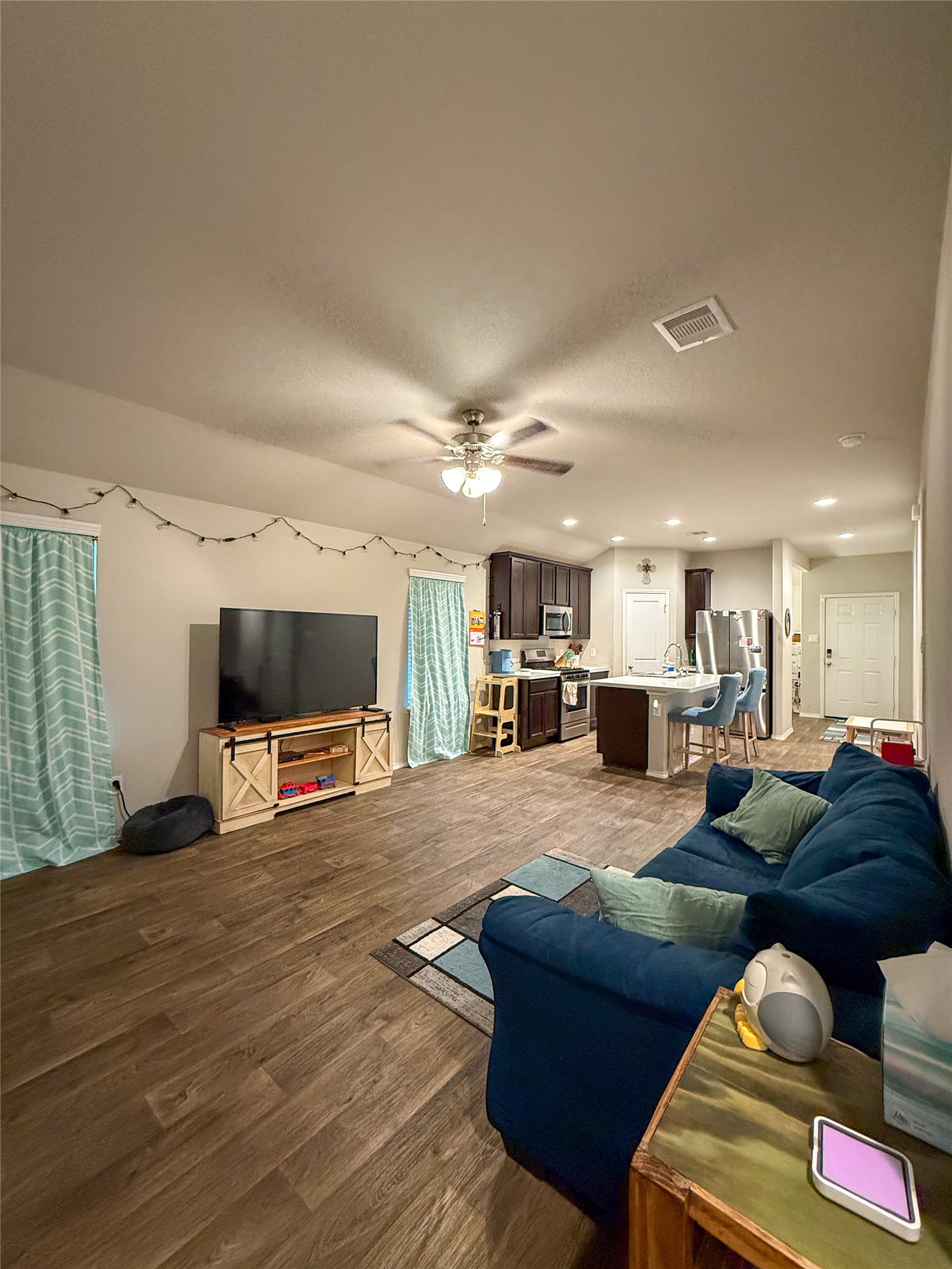 706 Zinnia Court Rosharon, TX 77583 - Photo 3 of 13 This photo showcases an open-concept living space with vinyl wood flooring, combining a cozy living room and a modern kitchen. The room features a ceiling fan and ample natural light, providing a comfortable and inviting atmosphere.