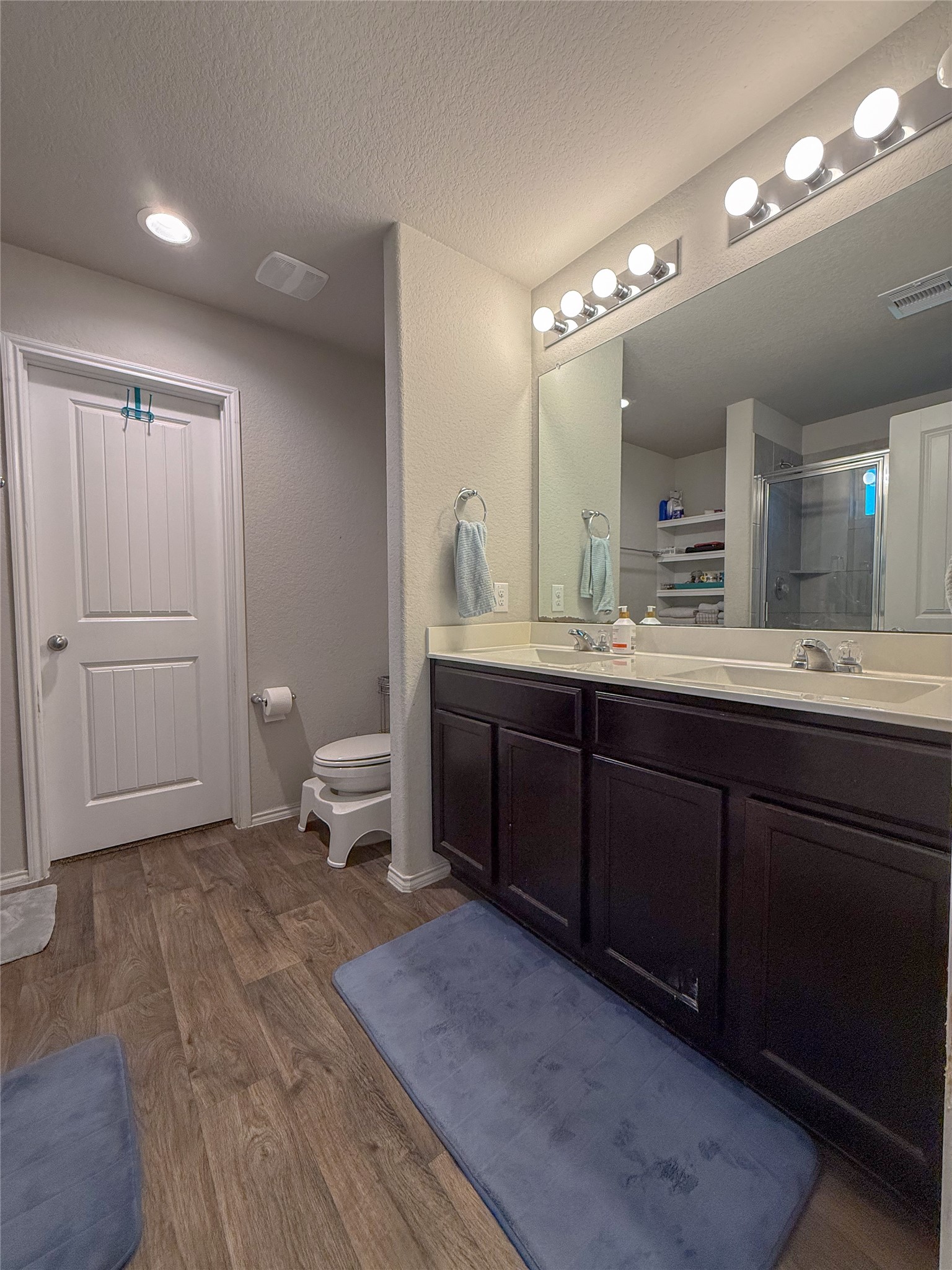706 Zinnia Court Rosharon, TX 77583 - Photo 10 of 13 This bathroom features a modern design with wood-look flooring, a dual-sink vanity with dark cabinetry, and a large mirror. It includes a shower enclosure and is well-lit with overhead lighting.