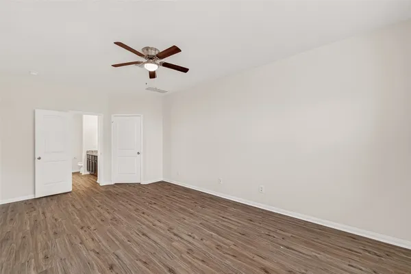an empty room with wooden floor ceiling fan and windows