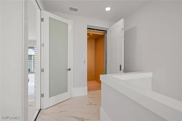 a view of a elevator and an empty room with wooden floor