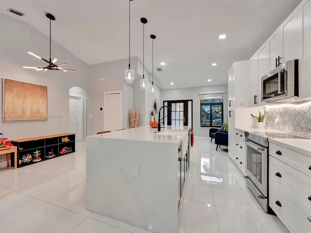a large white kitchen with kitchen island a stove a sink a center island and furniture