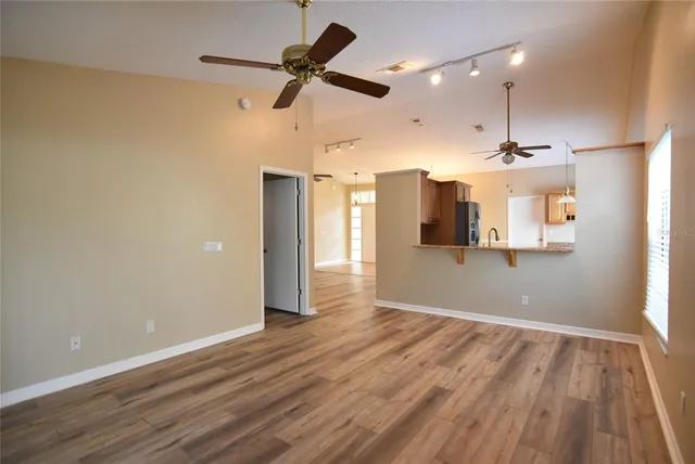 a view of a big room with wooden floor a ceiling fan and kitchen view