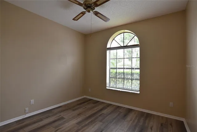an empty room with wooden floor fan and windows