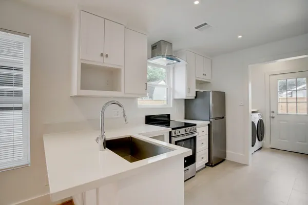 a kitchen with stainless steel appliances a stove a refrigerator sink and white cabinets with wooden floor