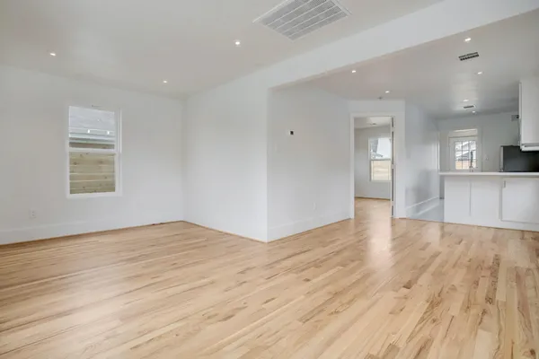 a view of empty room with wooden floor and kitchen view