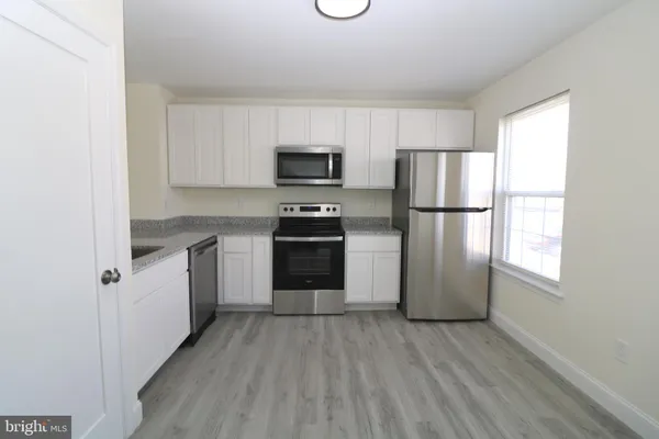 a kitchen with a refrigerator a stove top oven a refrigerator and white cabinets with wooden floor