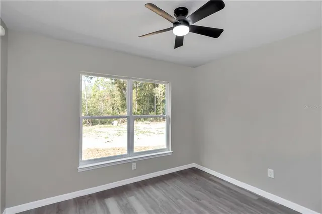 an empty room with wooden floor ceiling fan and windows